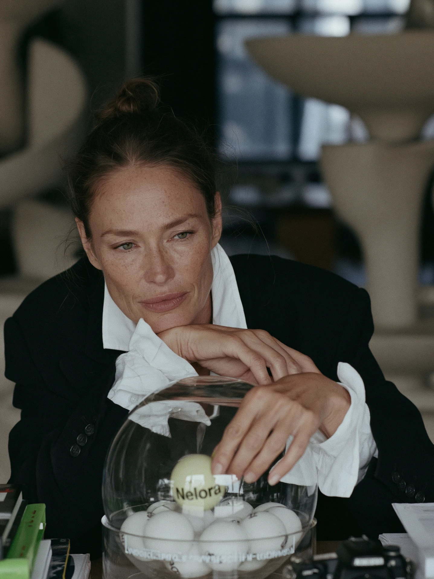 Woman resting her chin on her hand, drawing a ball labelled Nelora from a glass bowl of lottery balls